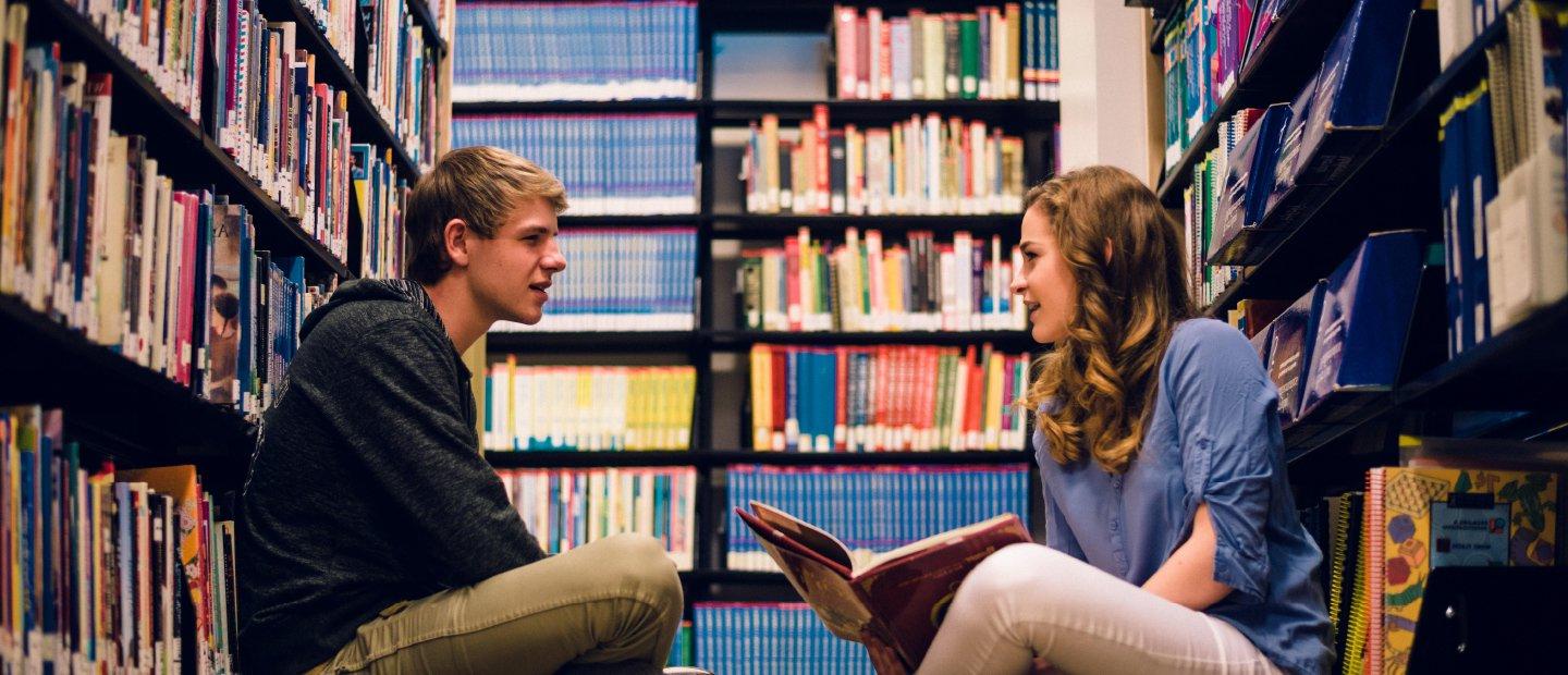 在图书馆里，男学生和女学生坐在地板上读书